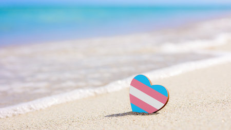Transgender flag in the shape of a heart on the sandy beach against the background of the sea.の写真素材