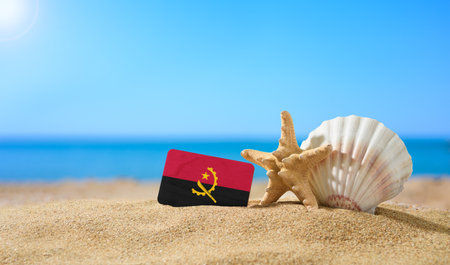 Tropical beach with seashells and Angola flag. The concept of a paradise vacation on the beaches of Angola.の写真素材