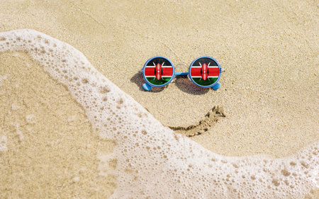Sunglasses with flag of Kenya on a sandy beach. Nearby is a sea lightning and a painted smile. The concept of a successful vacation in the resorts of the Kenya.の写真素材