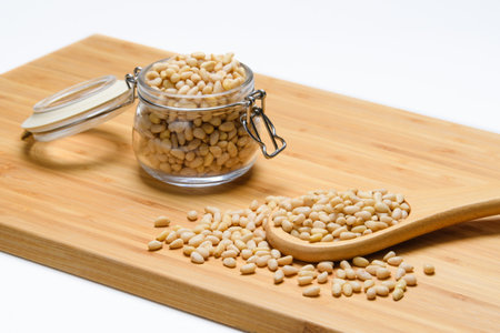 Pine nuts on a wooden board. Wooden spoon with pine nuts on the background of a jar of nuts. Selective background on a spoon with nutsの写真素材