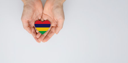 The national flag of Mauritius in the shape of a heart of arms in female hands. Flat lay, copy space.の写真素材
