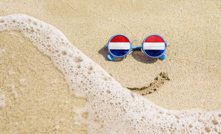 Sunglasses with flag of the Netherlands on a sandy beach. Nearby is a sea lightning and a painted smile.の写真素材