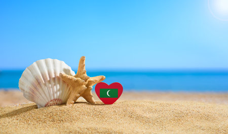 Maldives flag in the shape of a heart and shells on a sandy beach.の写真素材