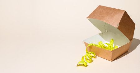 The concept of diet and the rejection of fast food. Measuring tape and hamburger container on a light background. selective focus, copy spaceの写真素材