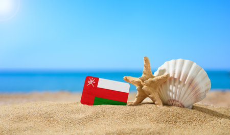Tropical beach with seashells and flag of Oman. The concept of a paradise vacation on the beaches of the Oman.の写真素材