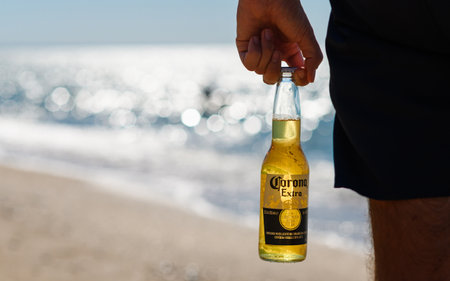 Anapa - Russia, August 2022: A bottle of Corona Extra beer in a man's hand against the backdrop of the evening sea. Selective focus on the logo. Relax concept.のeditorial素材