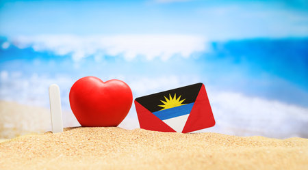 I love Antigua and Barbuda. Flag of Antigua and Barbuda on the beach with a red heart. Vacation and travel concept.の写真素材
