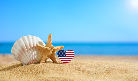 Beautiful beach of the coast of the United States. Flag of USA in the shape of a heart and shells on a sandy beach.の写真素材