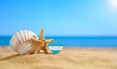 Beautiful beach in the Honduras. Flag of Honduras in the shape of a heart and shells on a sandy beach.の写真素材