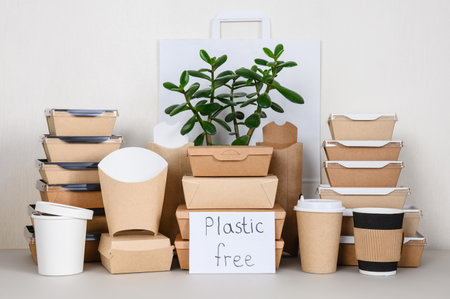 Plastic free inscription next to a set of eco-friendly food packaging. Disposable tableware made of paper and cardboard and a green plant.の写真素材