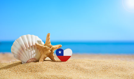 Beautiful beach in Chile. Chilean flag in the shape of a heart and seashells on a sandy beachの写真素材