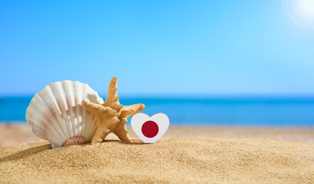 Beautiful beach of Japan. Flag of Japan in the shape of a heart and shells on a sandy beach.の写真素材