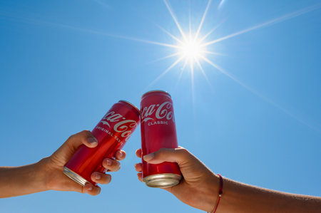 Anapa, Russia - July 30, 2023: Two cans of Coca-Cola in the hands of friends against the backdrop of the sun on a summer day.のeditorial素材