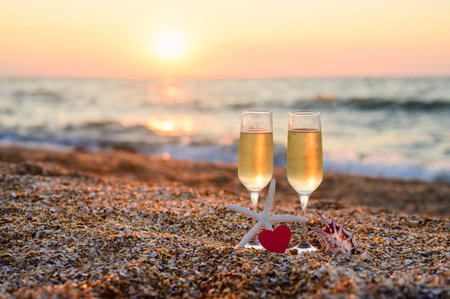 Glasses of wine and a red heart on the seashore. Romantic evening on the beach. Horizontal postcard, selective focusの写真素材