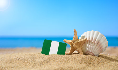 Tropical beach with seashells and Nigeria flag. The concept of a paradise vacation on the beaches of Nigeriaの写真素材