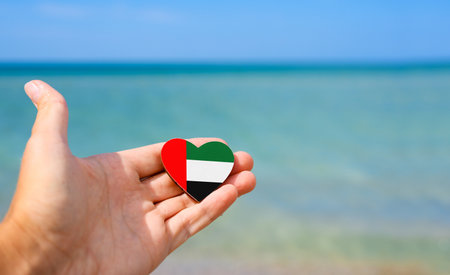 United Arab Emirates flag in hand with sea in background. Summer vacation in United Arab Emiratesの写真素材