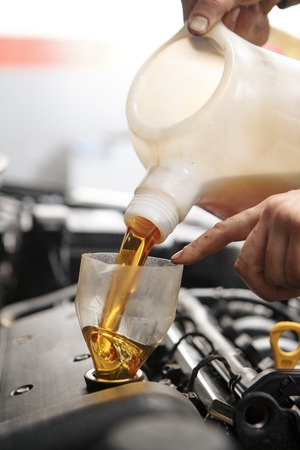 Car mechanic replacing and pouring fresh oil into engine at maintenance repair service stationの写真素材