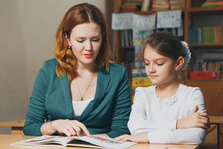 Female private tutor helping young student with homework at desk in bright childs roomの写真素材