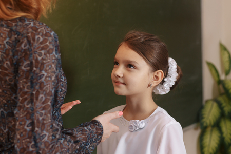 Happy schoolteacher helping a schoolgirl doing an addition on a blackboardの写真素材