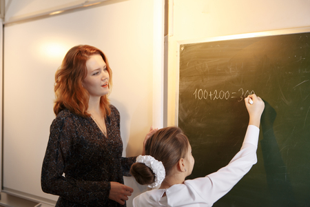 Happy schoolteacher helping a schoolgirl doing an addition on a blackboardの写真素材