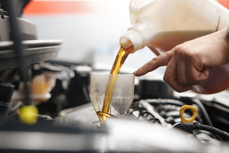 Car mechanic replacing and pouring fresh oil into engine at maintenance repair service stationの写真素材