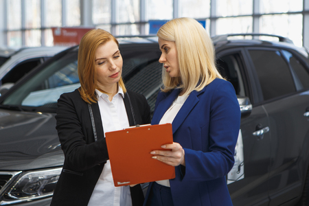 young woman is talking to handsome car dealership worker while choosing a car in dealershipの写真素材