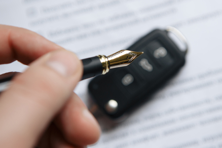 Man signing car insurance document or lease paper. Writing signature on contract or agreement. Buying or selling new or used vehicle. Car keys on table. Warranty or guarantee. Customer or salesman.の写真素材