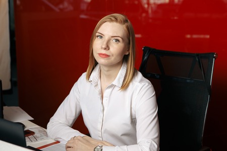 Beautiful and elegant woman head with red hair, looking in the diary talking on the smartphone with a subordinate, sitting at the office desk in the office on the background of documents.LIFESTYLEの写真素材