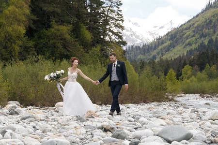 couple in wedding attire with a bouquet of flowers and greens is in the hands of a waterfall at sunset, the bride and groomの写真素材
