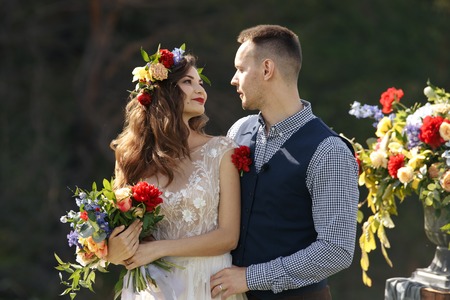 couple in wedding attire with a bouquet of flowers and greenery is in the hands against the backdrop of the field at sunset, the bride and groomの写真素材