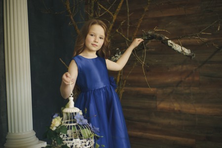 happy little girl holding decorative bird cage full of flowers. Studio shot in provence style interiorの写真素材