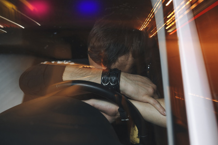 Upset male driver is caught driving under alcohol influence. Man covering his face from police car light.の写真素材