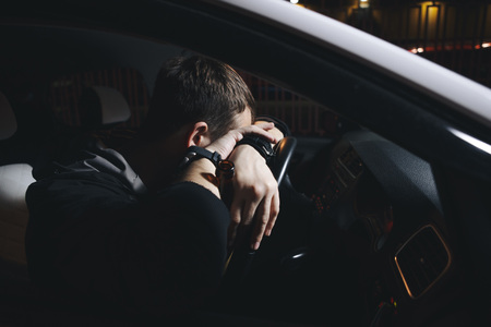 Male drunk driver drinking beer on the background of police car lighting. Driving under alcohol influenceの写真素材