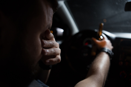 A bottle of alcohol in the hands of a man driving