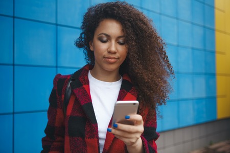 Smiling afro american woman using smartphone over blue backgroundの写真素材