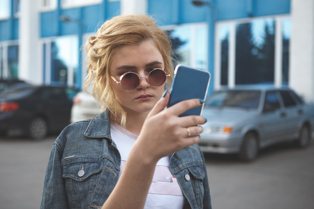 Worried teenager girl looking at her smart phone in a park with an unfocused backgroundの写真素材