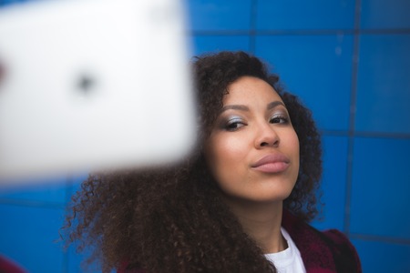 Close up portrait of cute excited latin girl making selfie with camera of her pda. She is in casual closes, has a beaming smileの写真素材