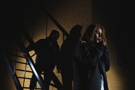 Criminal observing young woman walking alone at nightの写真素材