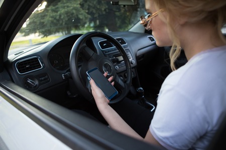 Business woman sitting in car and using her smartphone. Mockup image with female driver and phone...