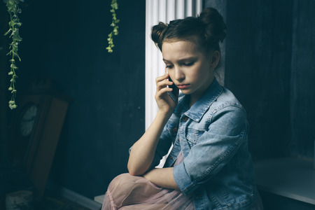 Unhappy teen girl looks at her smartphone experiencing anxiety and sad.