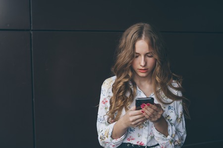 Unhappy teen girl looks at her smartphone experiencing anxiety and sad.の写真素材