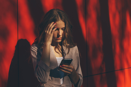 Unhappy young woman using smartphone portrait. Sad girl reading bad news or texting with mobile phone. Family issues, problem conceptの写真素材