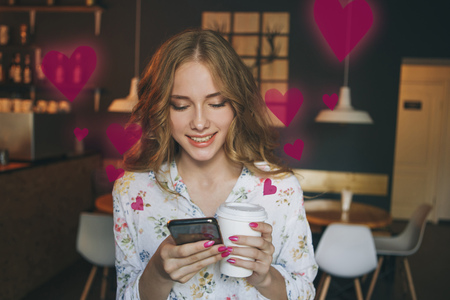 Woman typing write message on smart phone in a modern cafe. Cropped image of young pretty girl sitting at a table with coffee or cappuccino using mobile phone.の写真素材