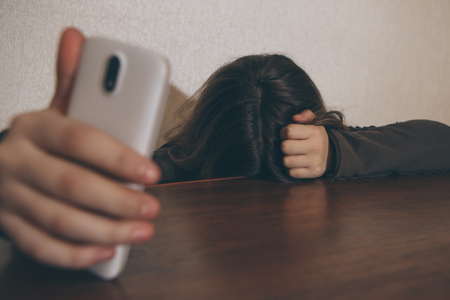 Teen girl excessively sitting at the phone at home. he is a victim of online bullying Stalker social networks - Imageの写真素材