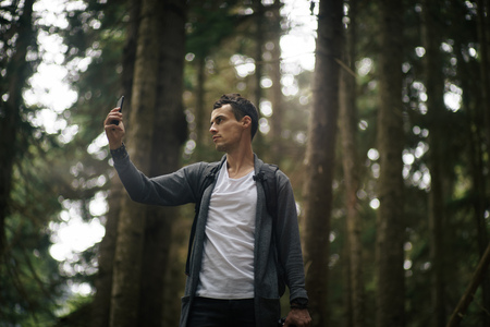 Self-confident man does selfie by the phone in the forest. Alone on the nature. Traveler lifestyle.の写真素材