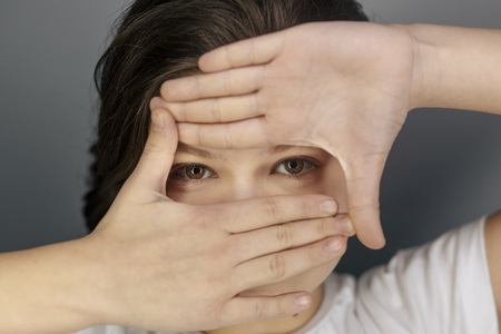 cheerful teen girl peeping surprised through hole in paperの写真素材