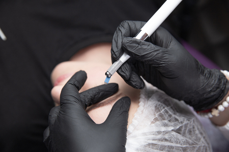 Permanent Makeup For Eyebrows. Microblading brow. Beautician Doing Eyebrow Tattooing For Female Face. Beautiful young girl in a beautyの写真素材