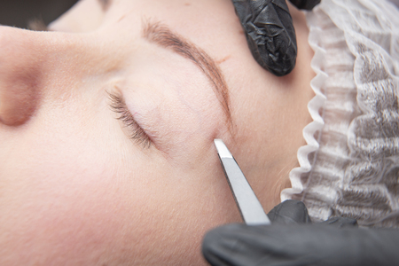 Young woman plucking eyebrows with tweezers closeの写真素材