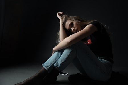 young scared and worried teenager girl holding mobile phone as internet stalked victim abused and...