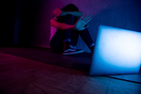 sad and scared female teenager with computer laptop suffering cyberbullying and harassment being online abused by stalker or gossip feeling desperate and humiliated in cyber bullyingの写真素材